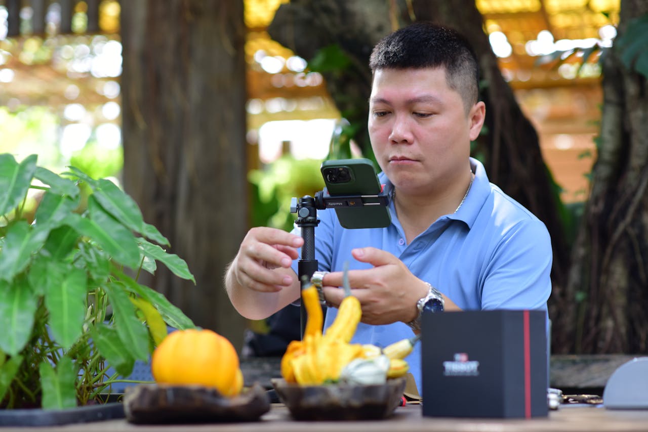 Adult man arranging a smartphone on a tripod outdoors for a nature-themed tabletop photoshoot.